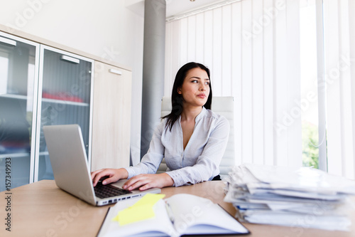 Attractive businesswoman looking trhougt window of her office while shes typing on laptop