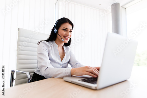 Attractive woman talking with customer at her work desk with headset photo