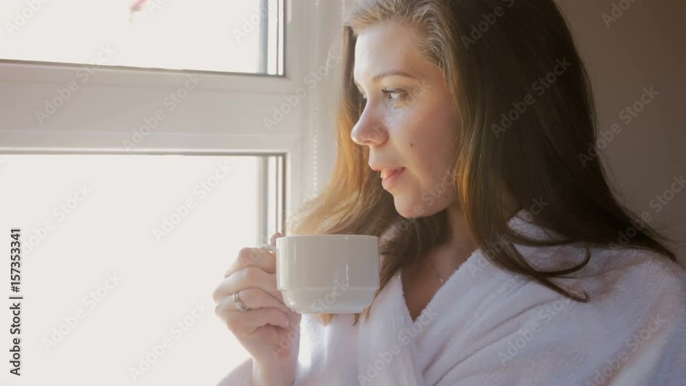 4k closeup video of beautiful young woman in bathrobe drinking coffee at window 4k closeup video of beautiful young woman in bathrobe drinking coffee at window