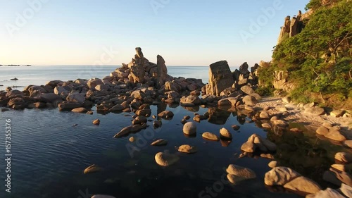 Yellow summer sunrise Aerial drone forward flight above sea water Kekura standing rock stones reflection in the ocean. Unique Far East of Russia natural monument. 4k photo