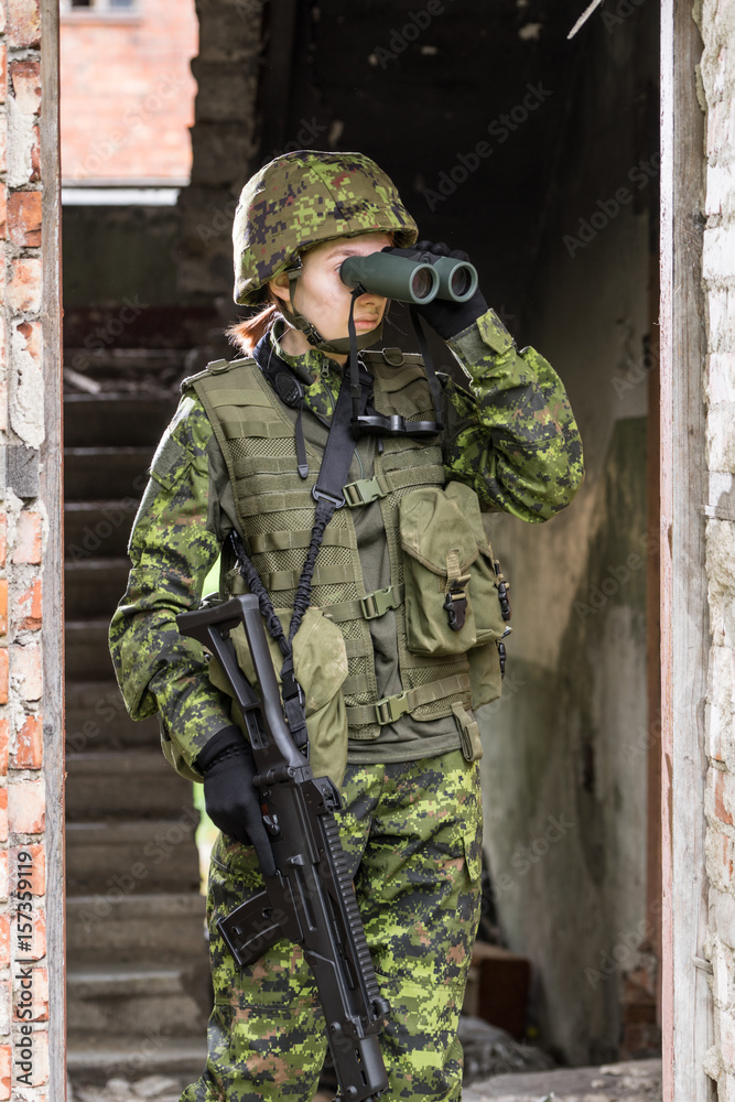 Portrait of armed woman with camouflage. Young female soldier observe with binoculars. Child soldier with gun in war, house ruins background. Military, army people concept Portrait of armed woman with camouflage. Young female soldier observe with binoculars. Child soldier with gun in war, house ruins background. Military, army people concept
