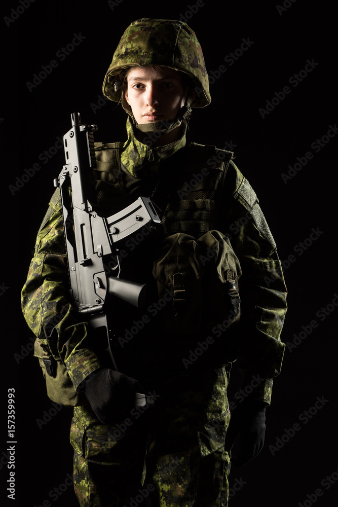 Portrait of armed woman with camouflage. Young female soldier observe with firearm. Child soldier with gun in war, black background.  Military, army people concept