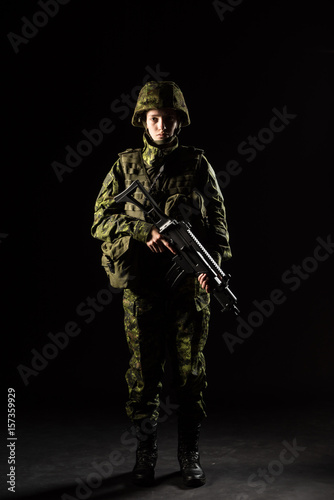 Portrait of armed woman with camouflage. Young female soldier observe with firearm. Child soldier with gun in war, black background.  Military, army people concept