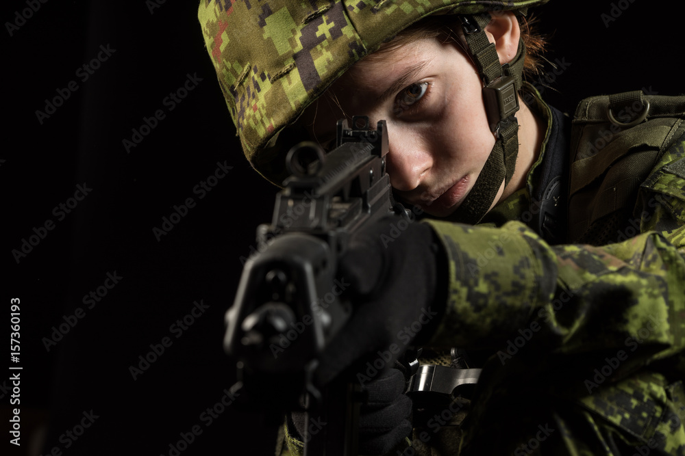 Portrait of armed woman with camouflage. Young female soldier observe with firearm. Child soldier with gun in war, black background.  Military, army people concept