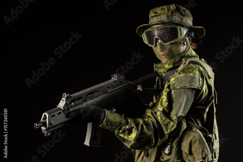 Portrait of armed woman with camouflage. Young female airsoft sniper observe with firearm. Soldier with gun in war, black background. Military, army people concept