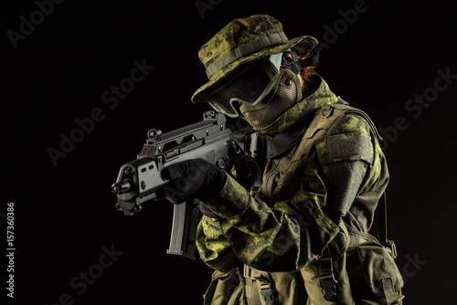 Portrait of armed woman with camouflage. Young female airsoft sniper observe with firearm. Soldier with gun in war, black background. Military, army people concept