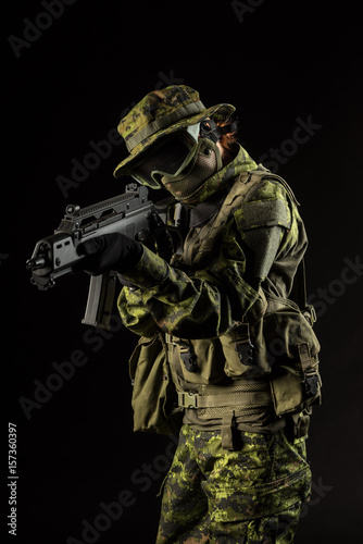 Portrait of armed woman with camouflage. Young female airsoft sniper observe with firearm. Soldier with gun in war, black background. Military, army people concept