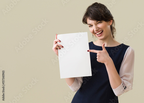 Portrait of young pretty business woman in white and blue suit shows piece of paper  on background.