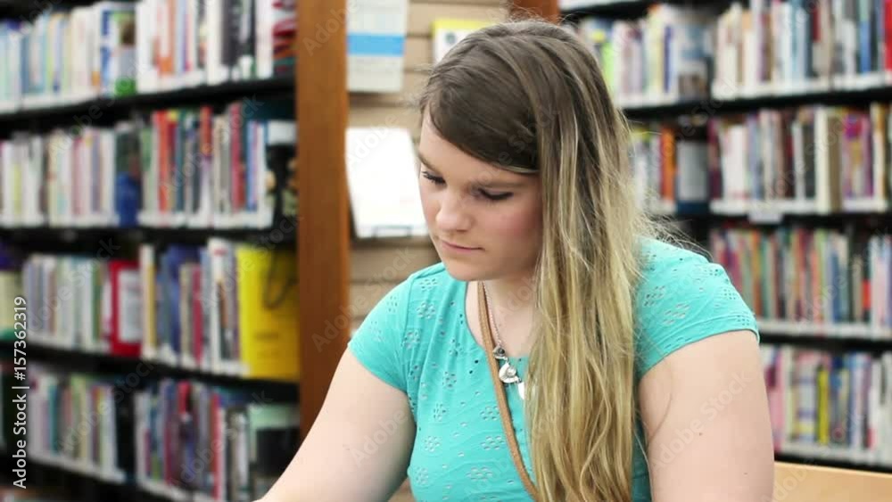Attractive blonde at library reading a book in an aisle - Angle 2 Attractive blonde at library reading a book in an aisle - Angle 2