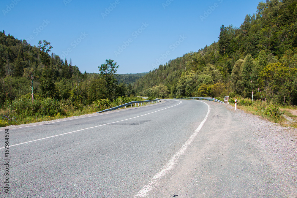 Road in mountain and trees around in a summer day