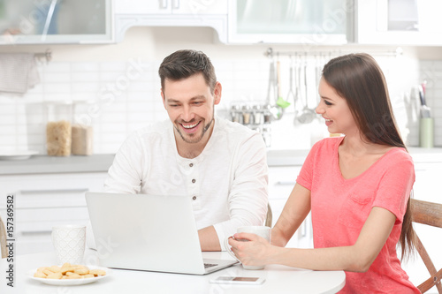 Young couple with laptop sitting at kitchen table
