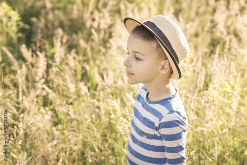 handsome boy stands in the grass field, a warm summer background behind him
