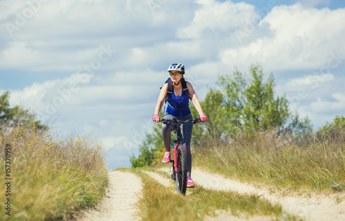 One young woman - an athlete rides on a mountain bike outside of town on the road in the forest on a summer day.