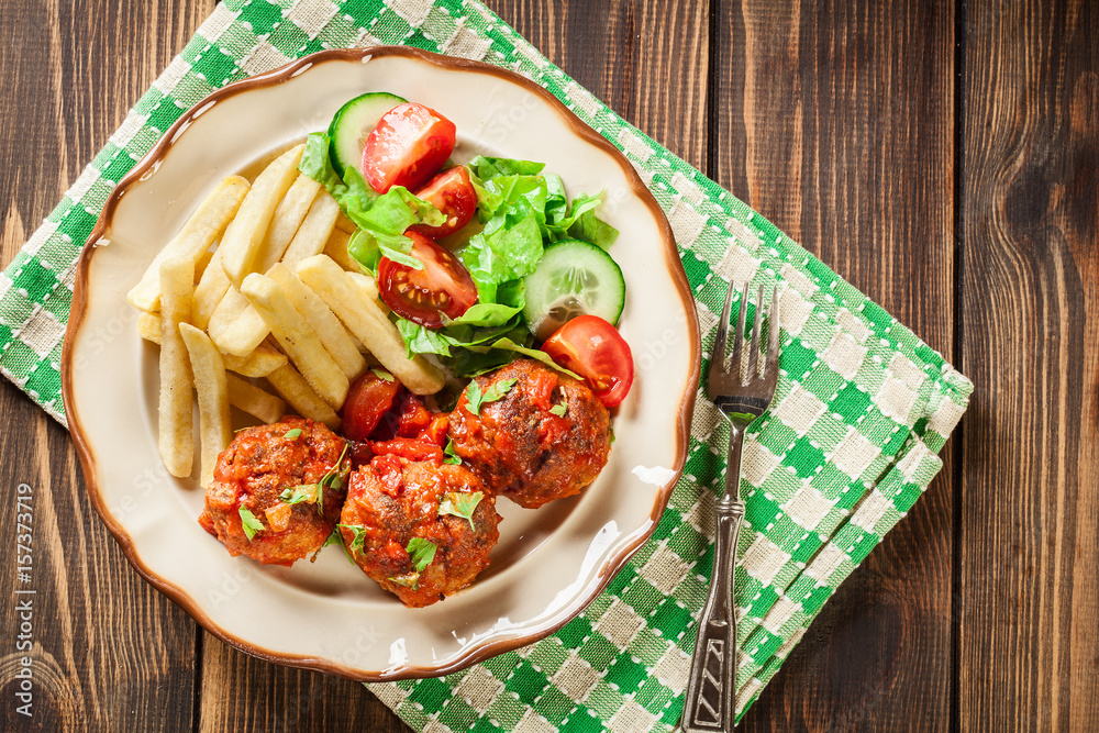 Roasted meatballs in tomato sauce with french fries and salad Roasted meatballs in tomato sauce with french fries and salad