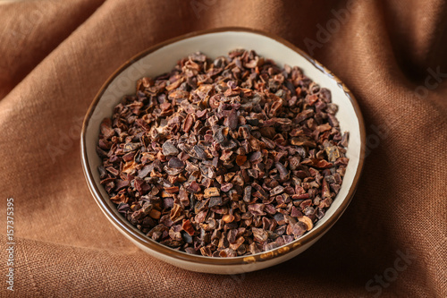 Bowl with cocoa nibs on brown cloth background