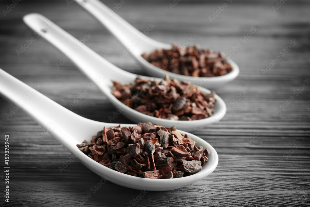 White spoons with cocoa nibs on wooden table White spoons with cocoa nibs on wooden table
