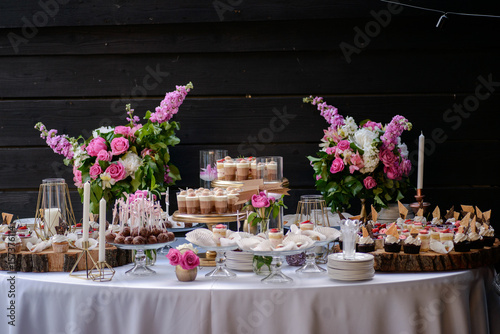 The wedding composition of delicious sponge fruit cakes decorated with juicy cherries and strawberries and are placed on the wooden table.