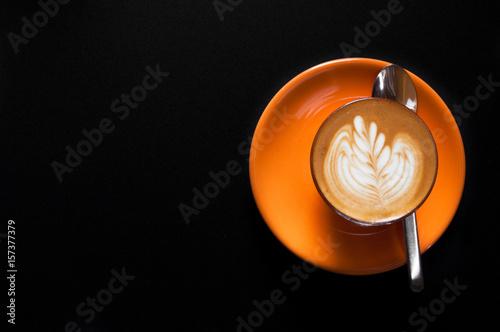 Hot latte in orange cup with floral pattern in foam on a dark background