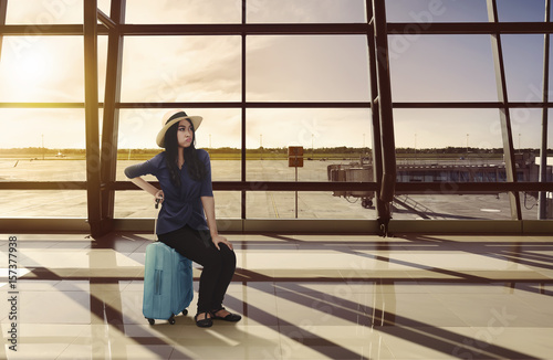 Tired asian traveler woman sitting on luggage waiting flight