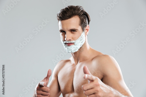 Young attractive man with shaving foam on face pointing