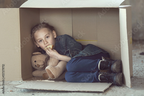 Poor little girl lying in cardboard box and eating bread