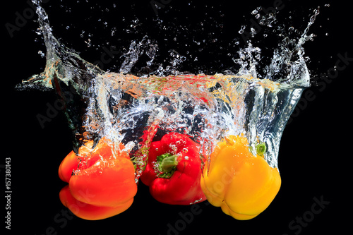 Red, orange and yellow peppers splashing water on black background photo