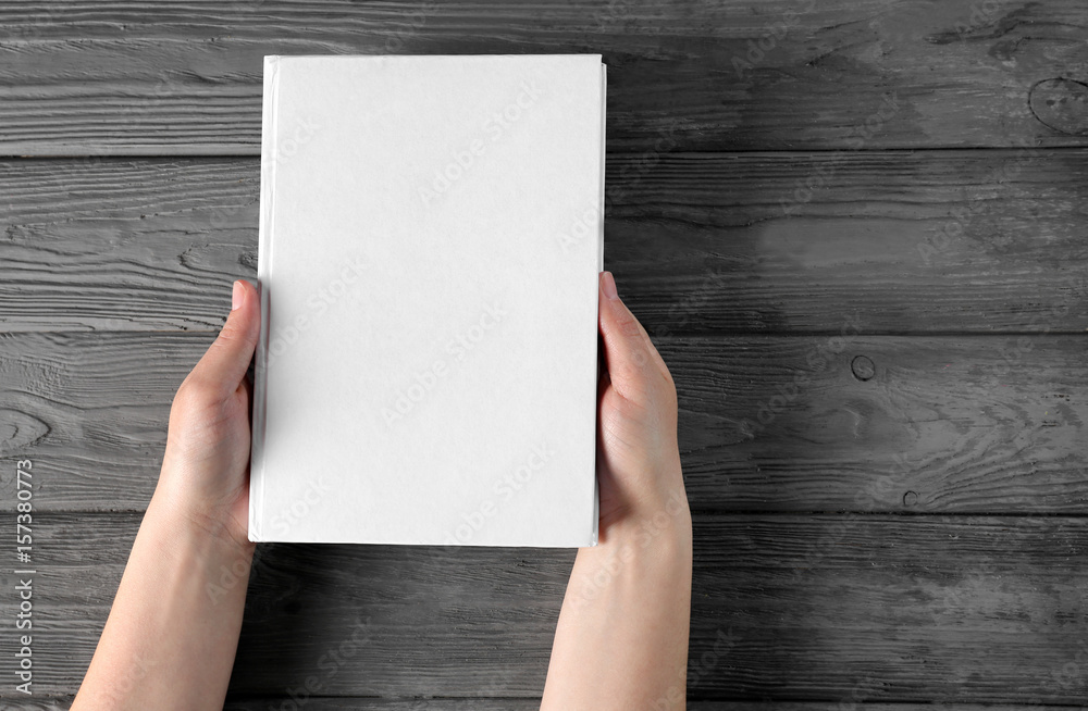 Female hands holding closed book with blank cover on wooden background Female hands holding closed book with blank cover on wooden background