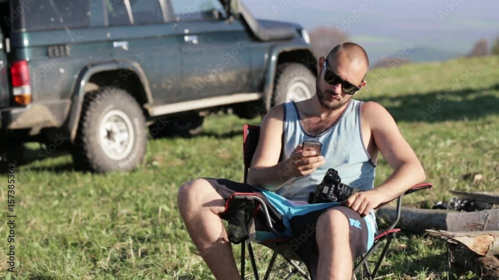 Tourist man sitting on the chair in camping with photo camera using smartphone Tourist man sitting on the chair in camping with photo camera using smartphone