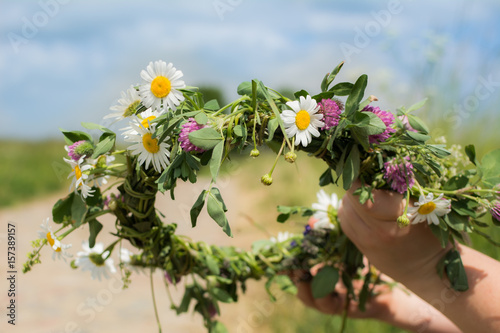 Fototapeta Naklejka Na Ścianę i Meble -  Hands making flower chain of chamomile and clover on sunny spring meadow with dirt road in the background.