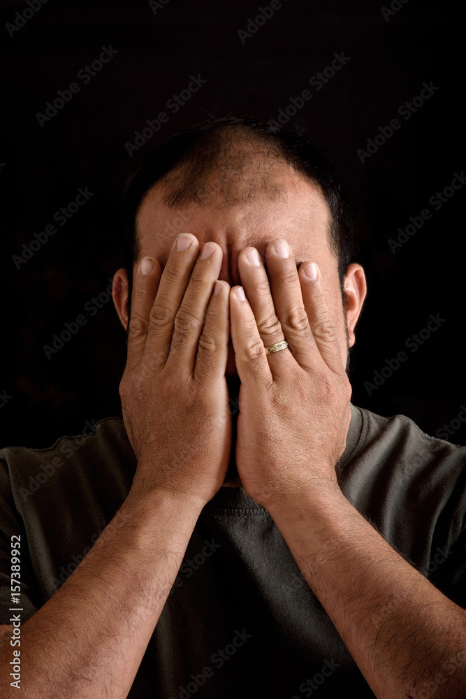 Man covering his face on black background Man covering his face on black background