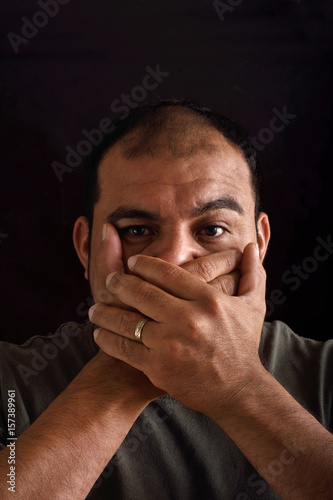 Man covering his mouth on black background
