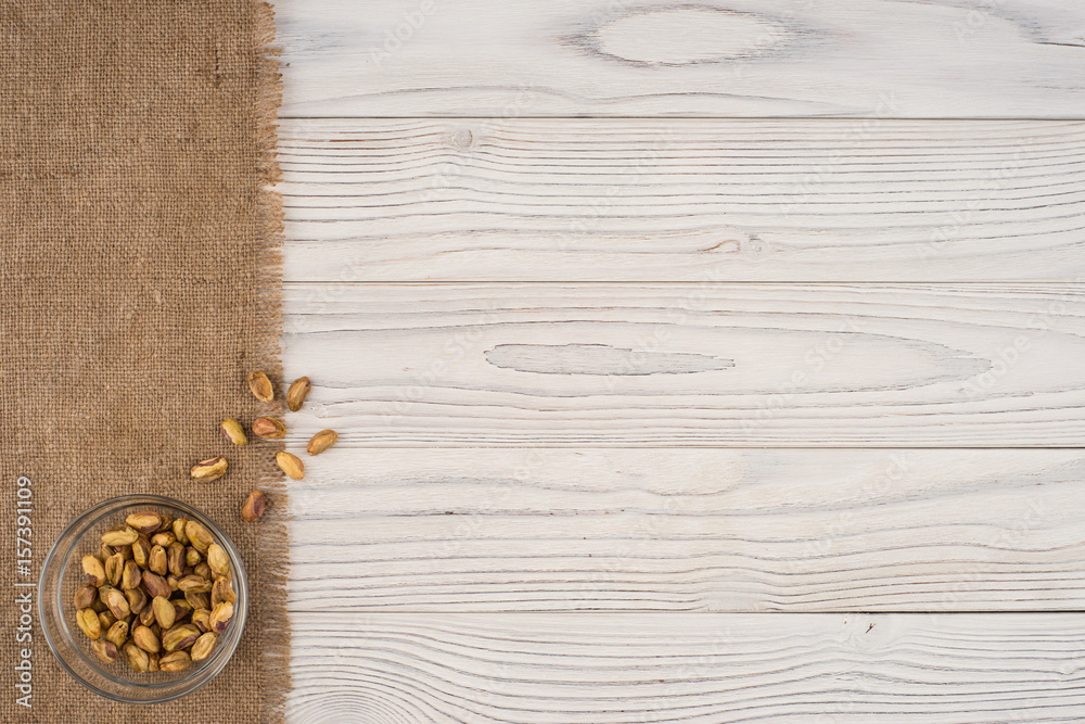 Pistachio nuts in a glass bowl on an old white wooden table.