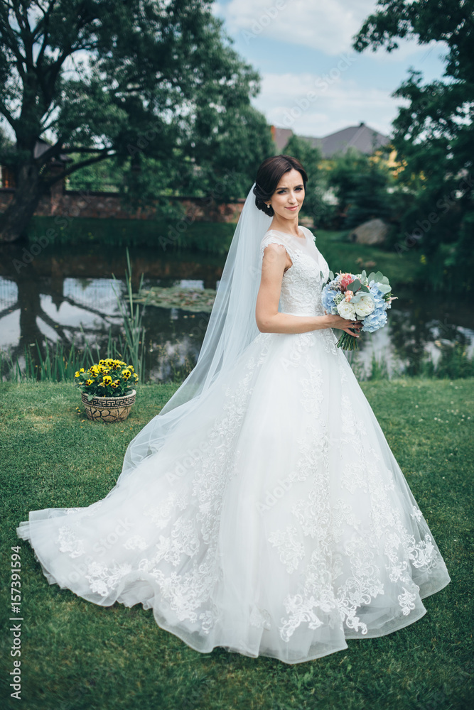 The charming bride keeps a wedding bouquet and stands on the yard
