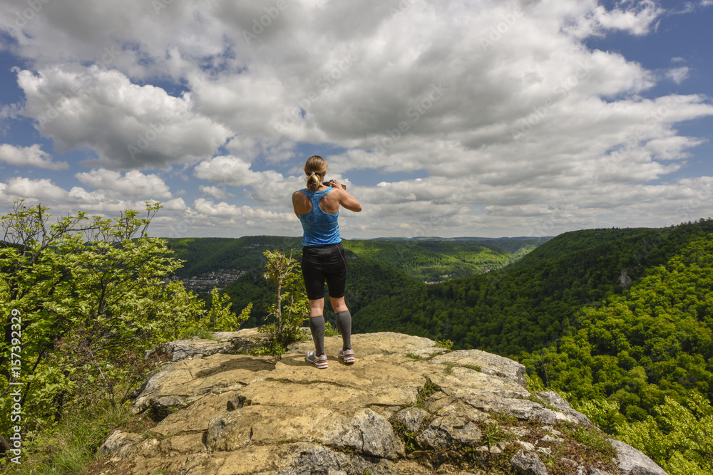 Sportive woman taking a photograph of a beautiful panorama, taking picture with mobile phone / handy / smartphone,  Bad Urach, Swabian Alps, Baden-Württemberg, Germany