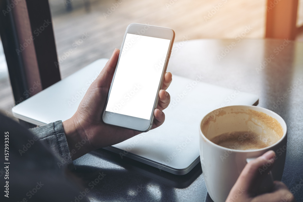 Mockup image of mobile phone with blank white screen with latop and coffee cup on wooden table in cafe