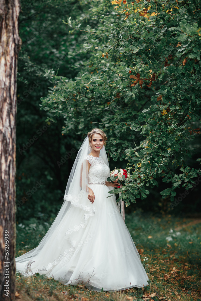 Bride with red wedding bouquet stands before a sick tree