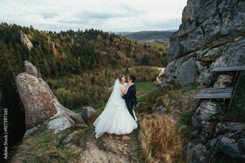 Wedding couple stands hugging on the rocks covered with green moss