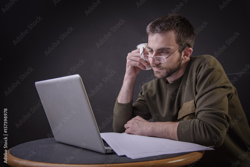 Young man enjoying his coffee and working on laptop, freelance writer or a blogger Young man enjoying his coffee and working on laptop, freelance writer or a blogger