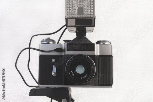 Old Soviet film camera on a tripod with a flash and a lens on a white background photo