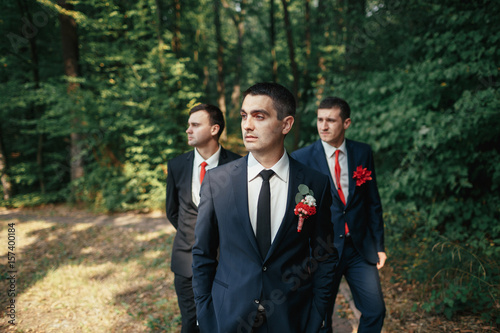 Groomsmen stand behind a groom in the forest
