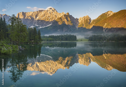 Panoramic view of beautiful white winter wonderland scenery in the Alps with mountain summits reflecting in crystal clear mountain lake on a colorful dawn