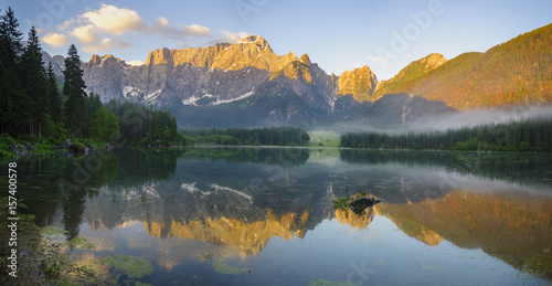 Panoramic view of beautiful white winter wonderland scenery in the Alps with mountain summits reflecting in crystal clear mountain lake on a colorful dawn