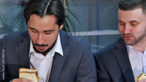 Two businessmen eating sandwich at lunch in office photo