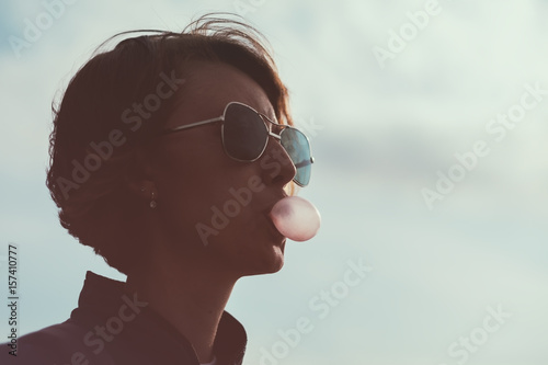 Murais de parede A girl wearing sunglasses blows a bubble of gum