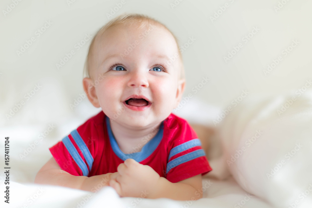 Happy adorable baby laughing and playing on soft white bed