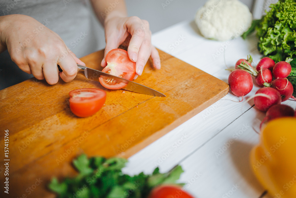 Woman hands cutting fresh red tomato on wooden board closeup. White table background. Woman hands cutting fresh red tomato on wooden board closeup. White table background.
