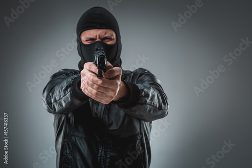 Burglar or terrorist in black mask shooting with gun.