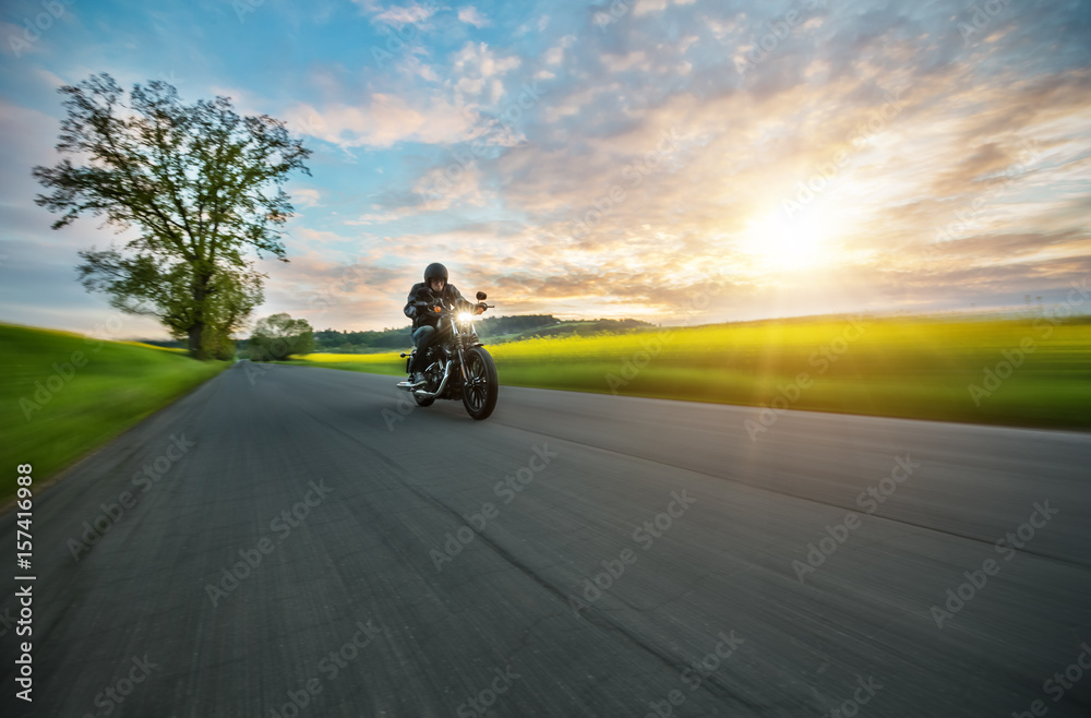Obraz premium Ciemny motocyklista jadący na motocyklu dużej mocy o zachodzie słońca
