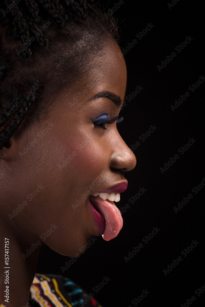 Smiling dark skinned model with sticking out tongue on a black background. close up portrait of