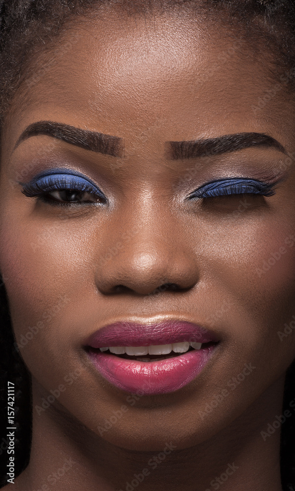 Close up portrait of dark skinned model with one eye closed. Smiling winking face of dark skinned young woman. Bright make up on dark skin. Close up portrait of dark skinned model with one eye closed. Smiling winking face of dark skinned young woman. Bright make up on dark skin.
